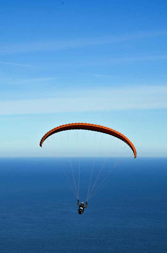 pexels photo 2127789 2127789 A person paragliding with an orange chute over a vast ocean under clear blue skies.